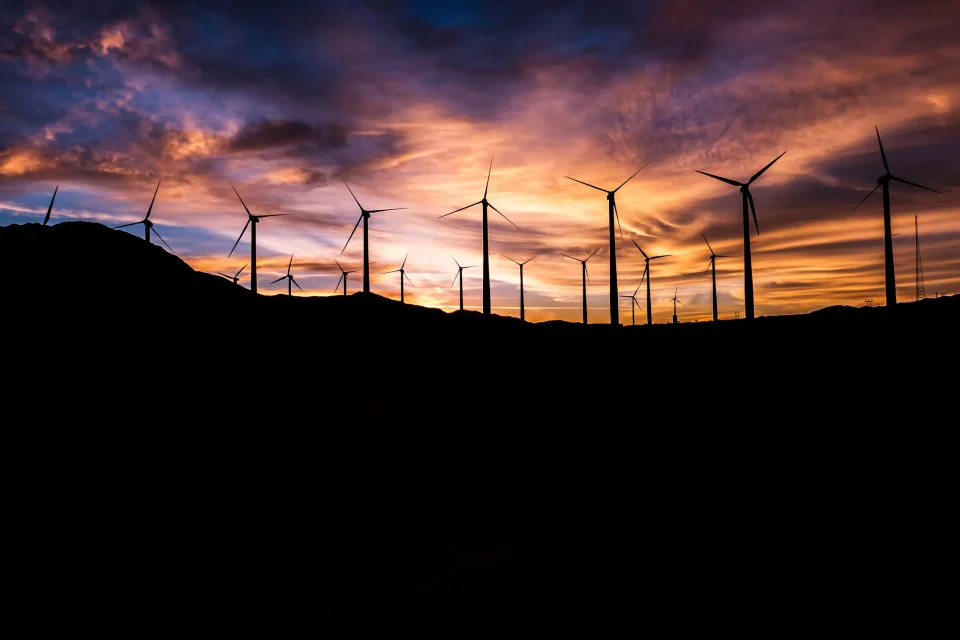 Wind turbines along the top of a hill with the sun setting behind. Photo by Master Wen