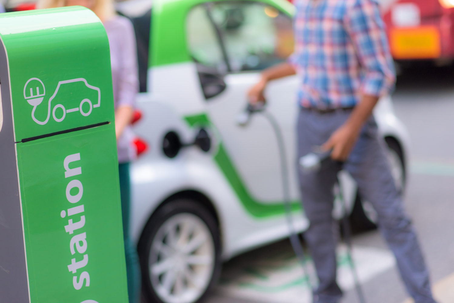 Man plugging Smart electric car by charging station in city