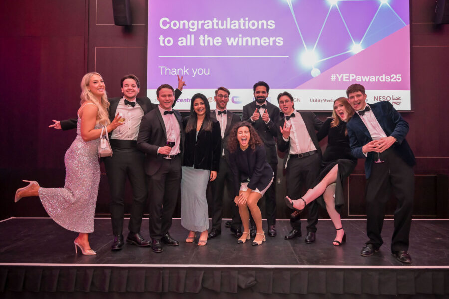 “A group of formally dressed attendees stand together on stage, leaning and posing playfully in front of a large screen displaying ‘Congratulations to all the winners’, ‘Thank you’, and ‘#YEPawards25’.”